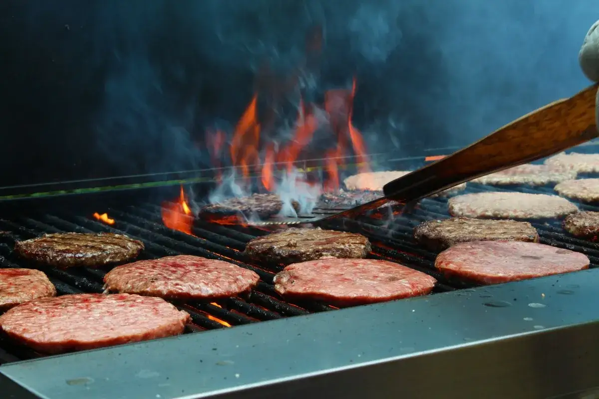 De nombreuses galettes de viande sur un barbecue, prêtes pour un festin. Le barbecue viande par personne est assuré !