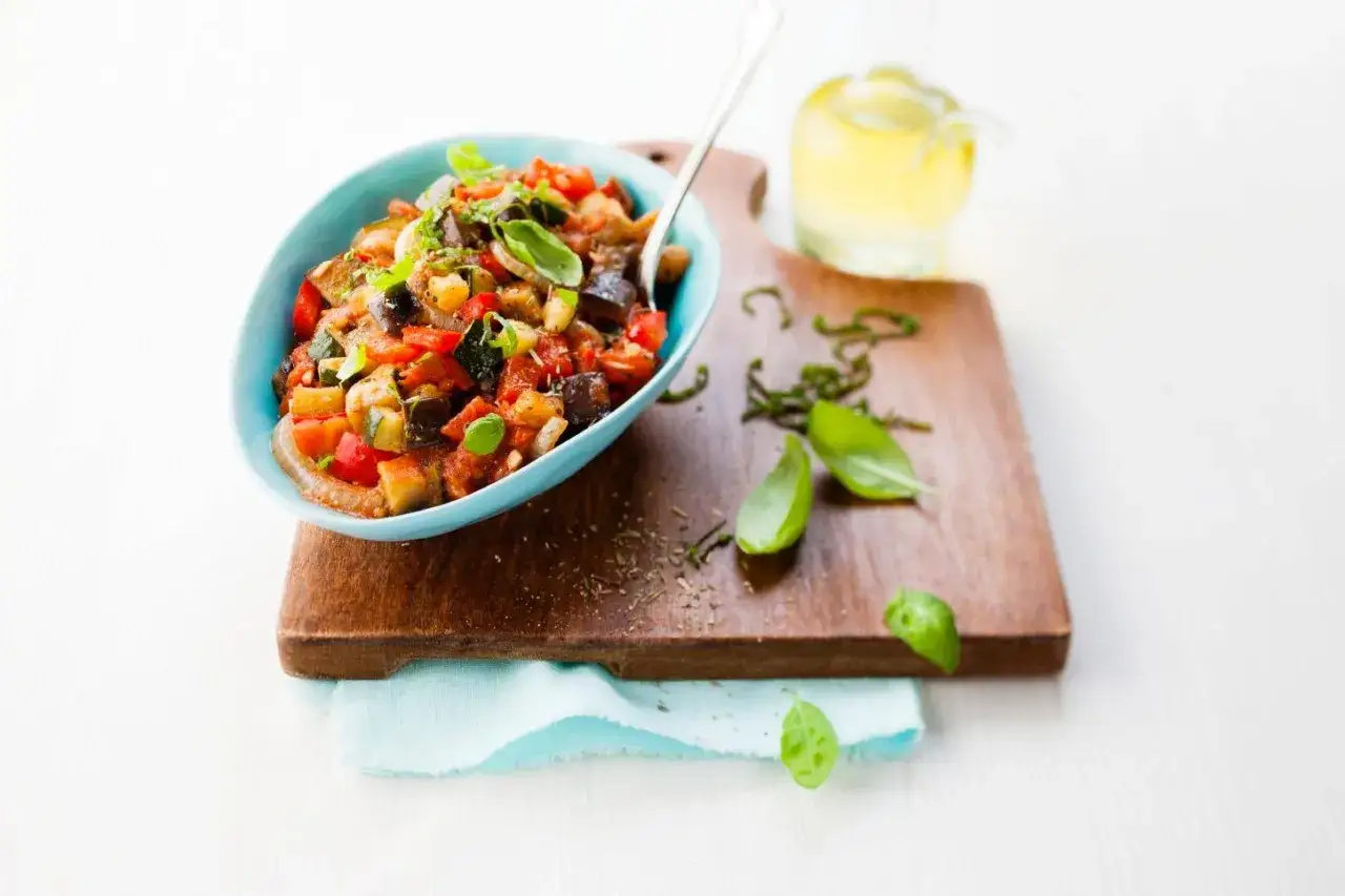 Un délicieux ratatouille Cookeo servi dans un bol bleu, garni de basilic frais.
