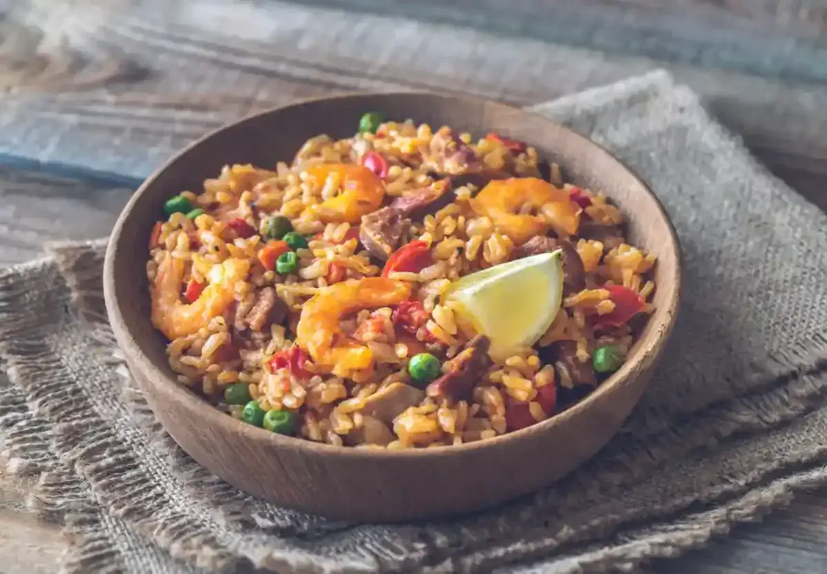 Un d&eacute;licieux paella cookeo, garni de crevettes, petits pois et chorizo, servi dans un bol en bois sur une toile de jute.