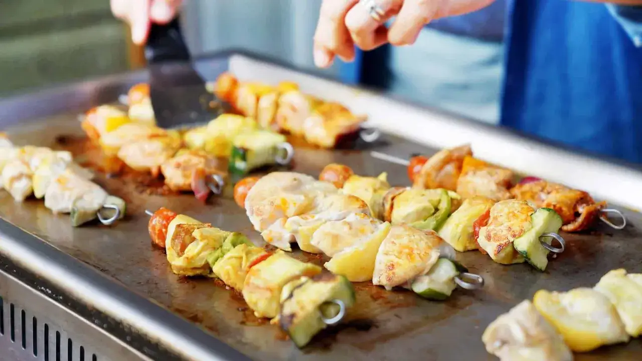 Brochettes de poulet et légumes grillant sur une plancha. Une excellente recette plancha pour un repas estival.