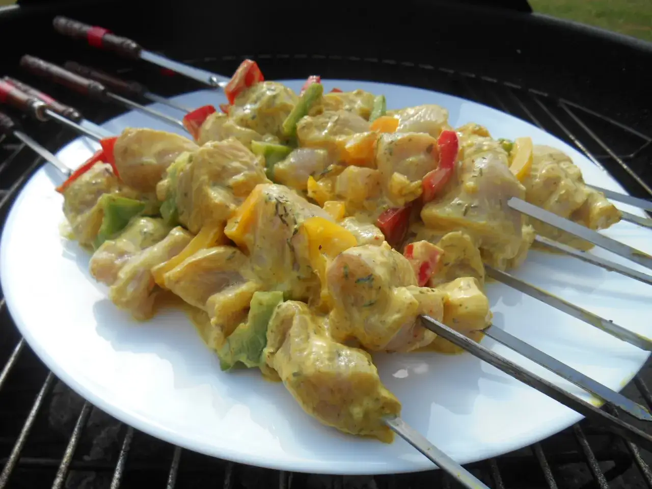 Brochettes de poulet marinées dans une sauce curry crémeuse, prêtes à être grillées.