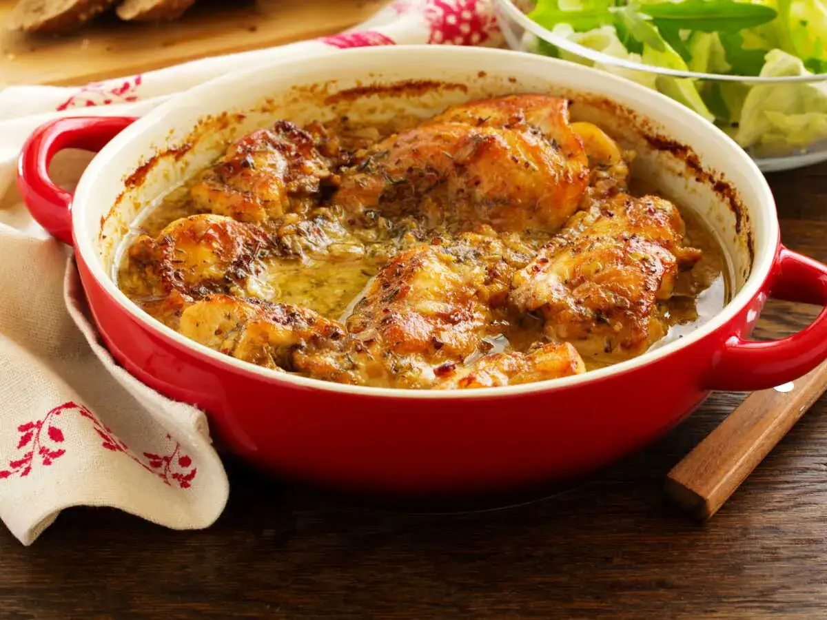 Un plat de lapin à la moutarde mijoté dans une cocotte rouge, servi avec une salade verte et du pain.