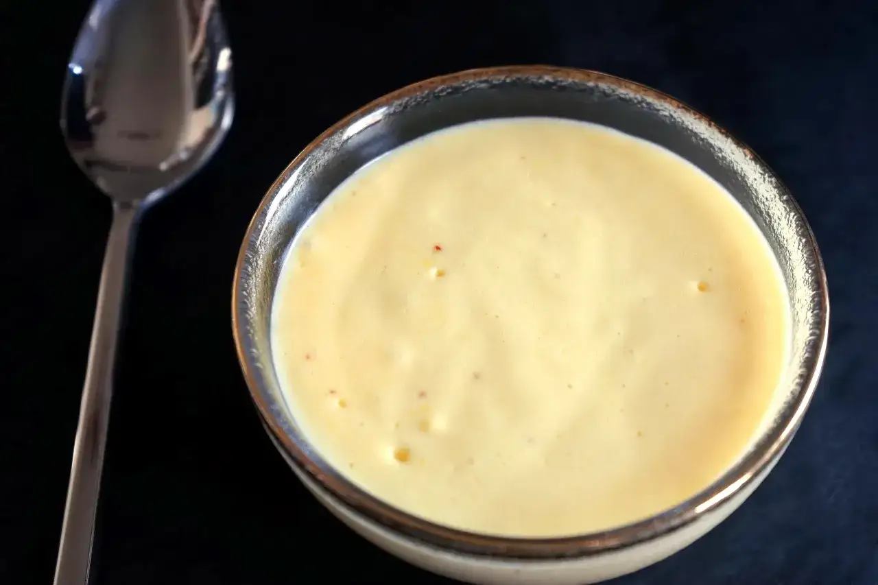 Un bol de sauce hollandaise onctueuse, prête à être dégustée avec une cuillère à proximité.