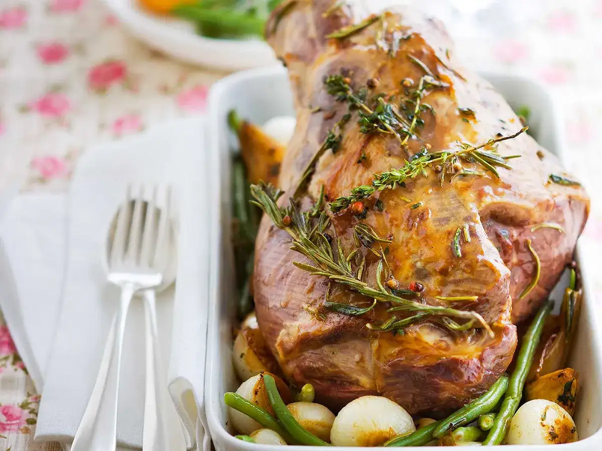 Gigot d'agneau rôti, parfumé au romarin et thym, servi avec des oignons et haricots verts. Une belle recette pour un repas de fête.
