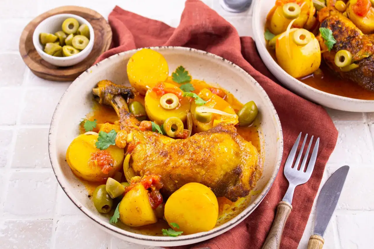 Un plat appétissant de tajine poulet citron, garni de pommes de terre, d'olives vertes et de coriandre fraîche.