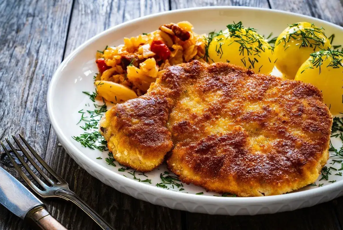 Un délicieux filet de poulet pané, servi avec des pommes de terre et une salade de chou.