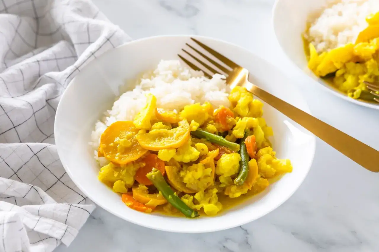 Un plat de riz blanc servi avec un curry de l&eacute;gumes color&eacute;, compos&eacute; de chou-fleur, carottes, courgettes et haricots verts.