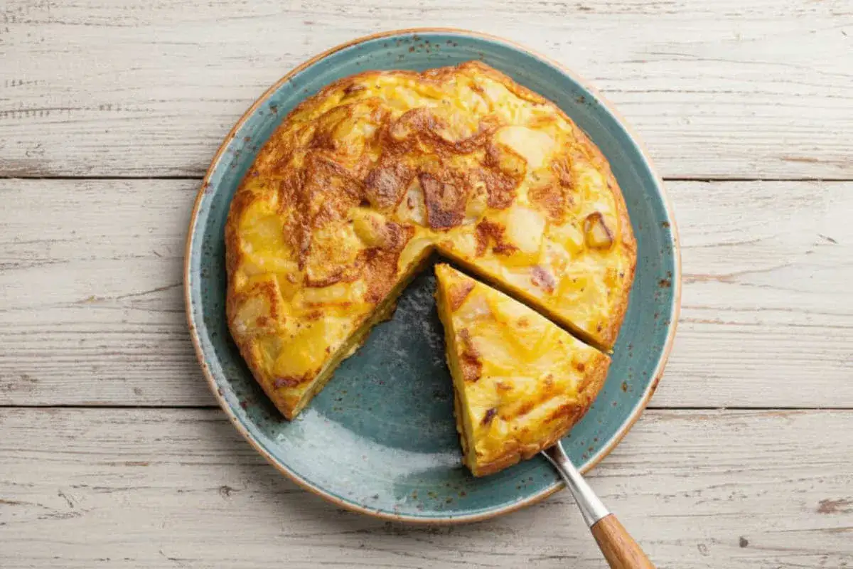 Une tranche de tortilla espagnole dorée, avec des pommes de terre et des œufs, est servie sur une assiette bleue.