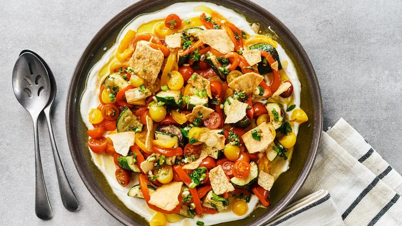 Salade color&eacute;e de courgette, tomate et poivron, garnie de pain pita croustillant et servie sur un lit de yaourt cr&eacute;meux.