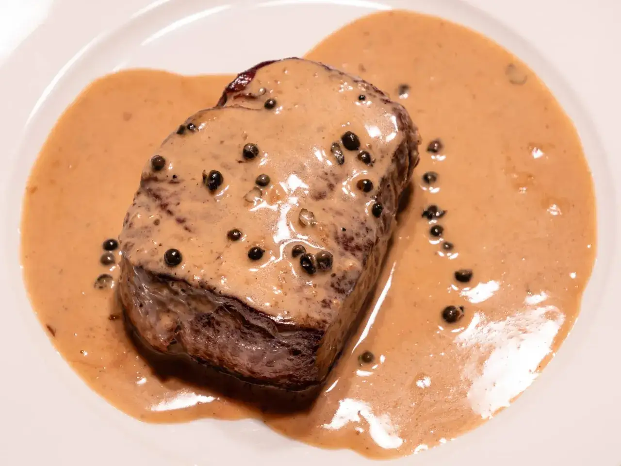 Un morceau de viande tendre nappé d'une onctueuse sauce au poivre, parsemée de grains de poivre noir. Un délice visuel et gustatif.