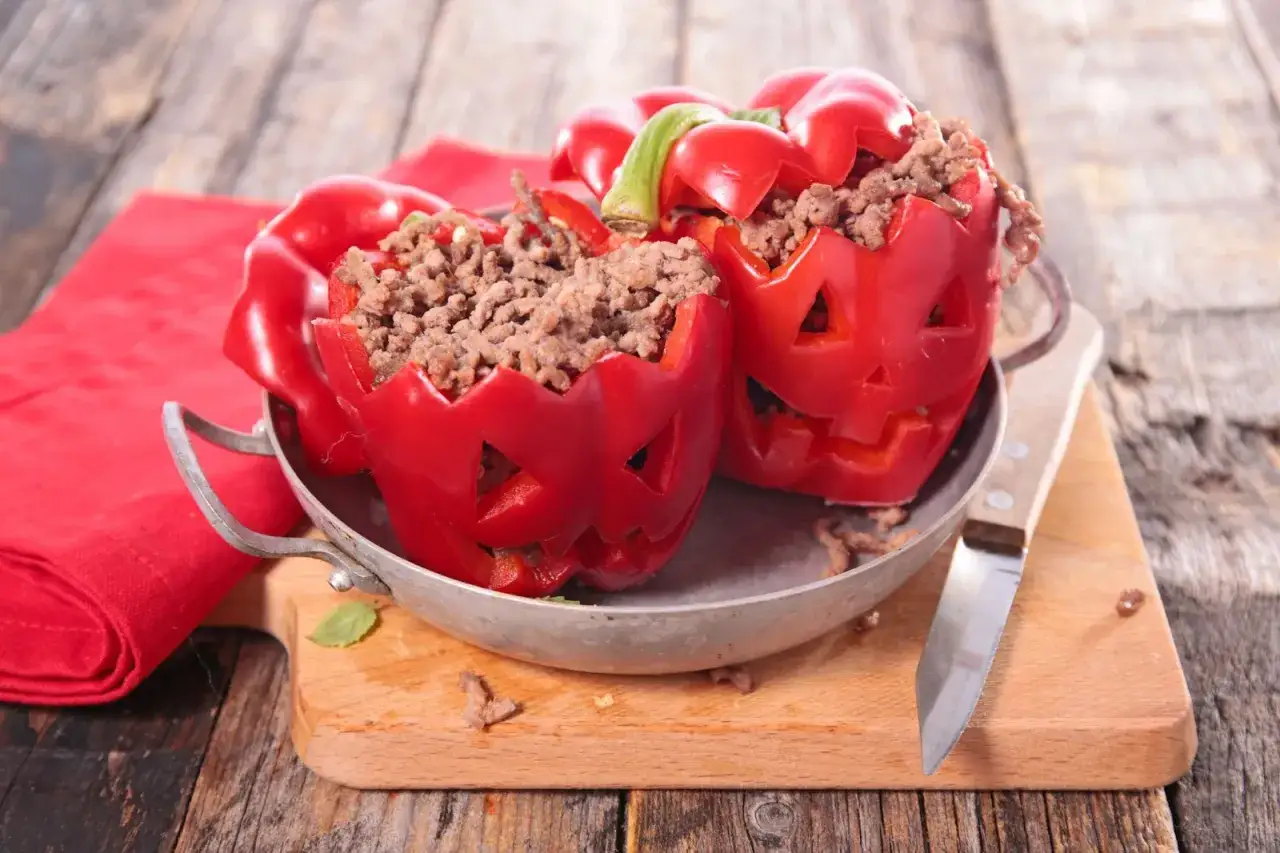 Deux poivrons rouges sculptés en citrouilles d'Halloween, remplis d'un délicieux plat à base de viande hachée. Parfait pour un repas effrayant et savoureux !