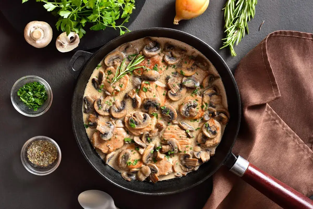Escalope de poulet à la crème et aux champignons, garnie de persil frais et d'une branche de romarin. Un plat savoureux prêt à être dégusté.