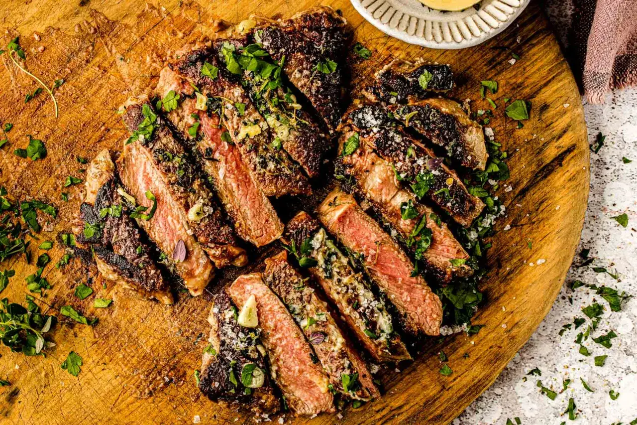 Tranches de bœuf barbecue juteuses, garnies d'herbes fraîches et d'ail, sur une planche en bois. Un délice pour les amateurs de viande.