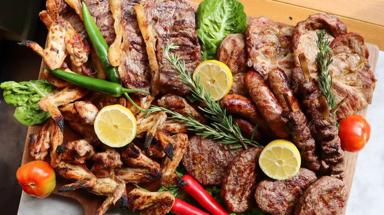 Un plateau généreux de barbecue italien : ailes de poulet, saucisses, steaks, brochettes, poivrons verts, citrons, tomates et romarin.
