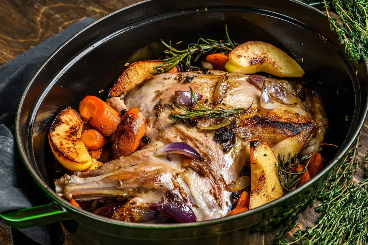 Un rôti de viande pour Pâques, doré et savoureux, mijoté avec des carottes, des pommes et des herbes aromatiques dans une cocotte.