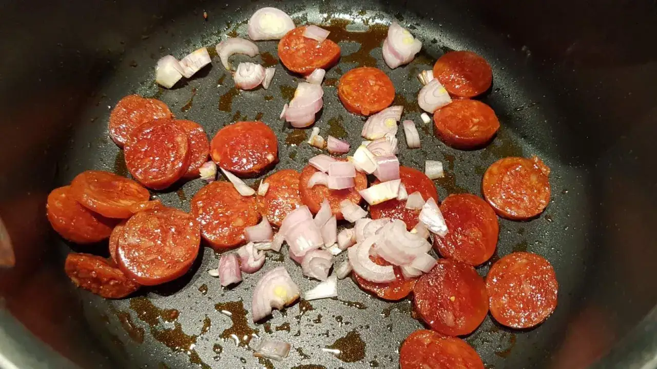 Rondelles de chorizo et échalotes coupées en dés dans une poêle, prêtes à devenir une délicieuse sauce chorizo.