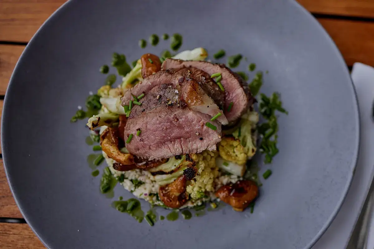 Tranches de gigot d'agneau juteux, sur un lit de chou-fleur rôti et de grains, arrosé d'une sauce verte. Un plat qui fait fondre en bouche, un vrai gigot qui pleure de plaisir.