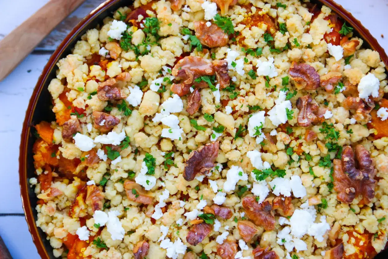 Un délicieux crumble de légumes, garni de noix croquantes et de fromage feta émietté, parsemé de persil frais.