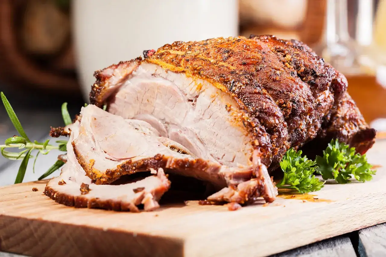 Un délicieux roti d'agneau au four, tranché et servi sur une planche en bois avec du romarin et du persil.