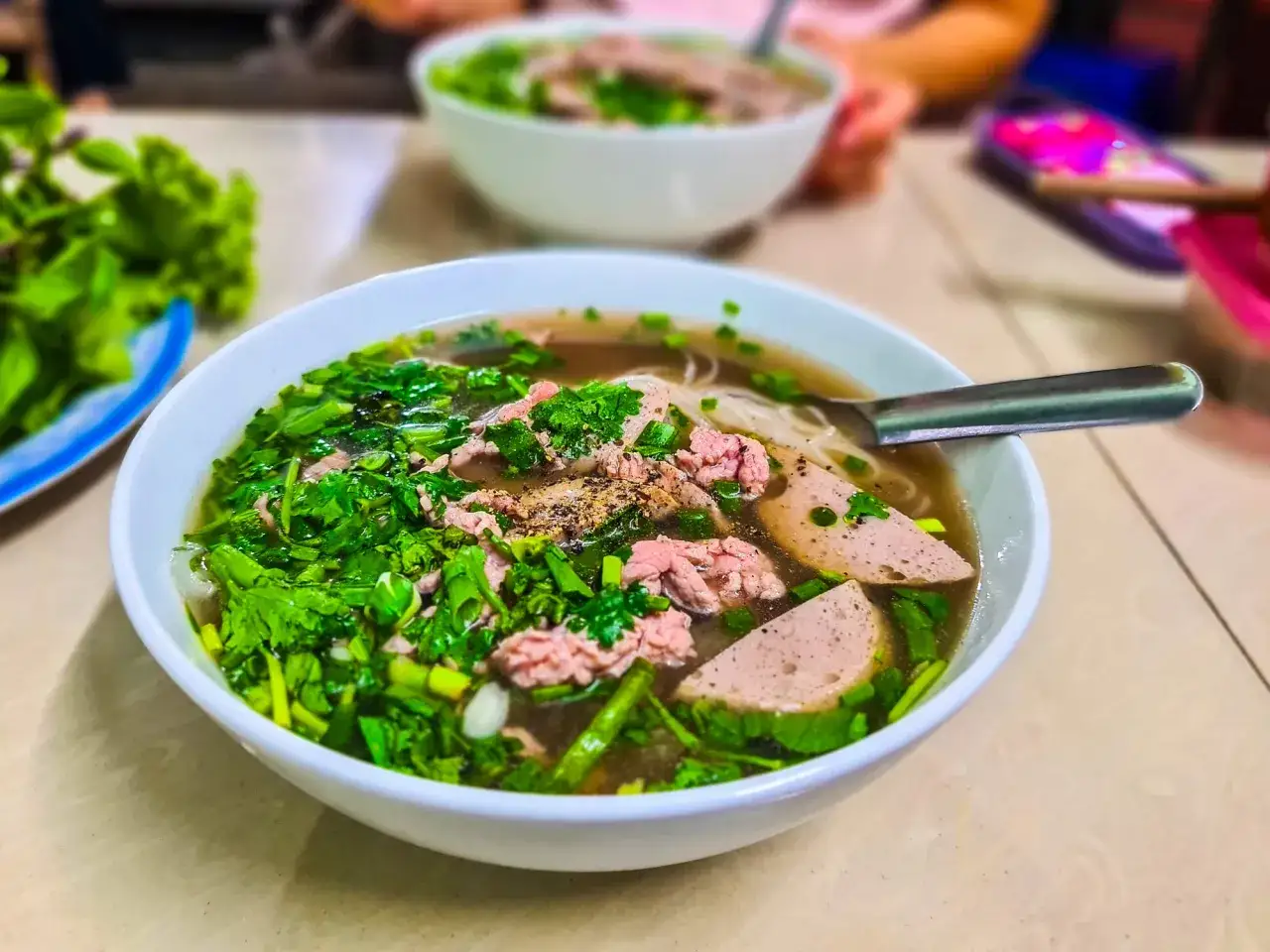 Un bol de soupe pho fumant, garni de fines tranches de bœuf, de saucisse et d'herbes fraîches. Un délice à savourer.