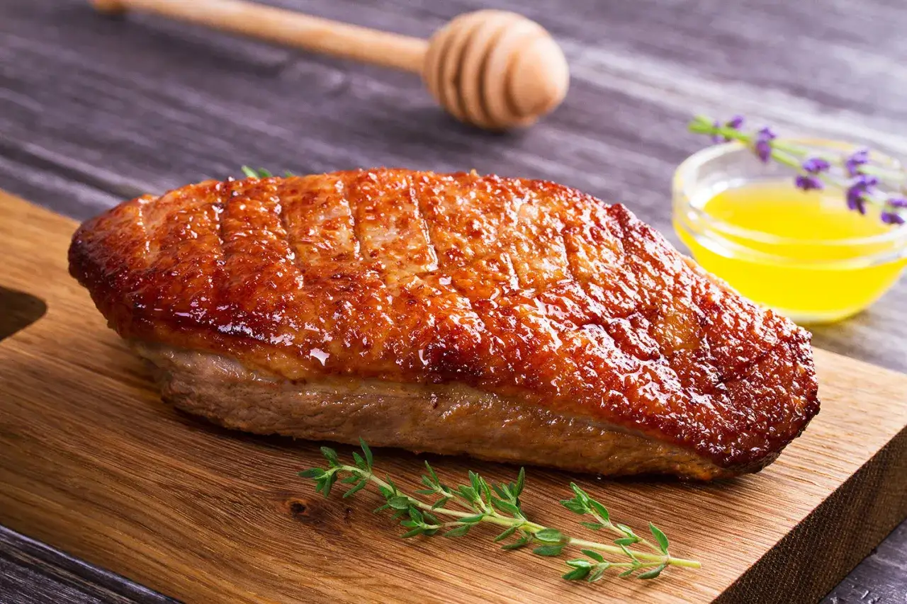Un magret de canard au four, la peau dorée et croustillante, servi sur une planche en bois avec du thym frais et une petite coupelle de sauce dorée.