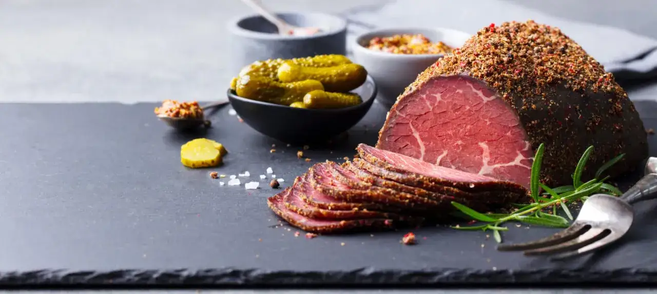 Tranche de pastrami épicé, cornichons, moutarde et sel. Une recette de pastrami qui donne envie.