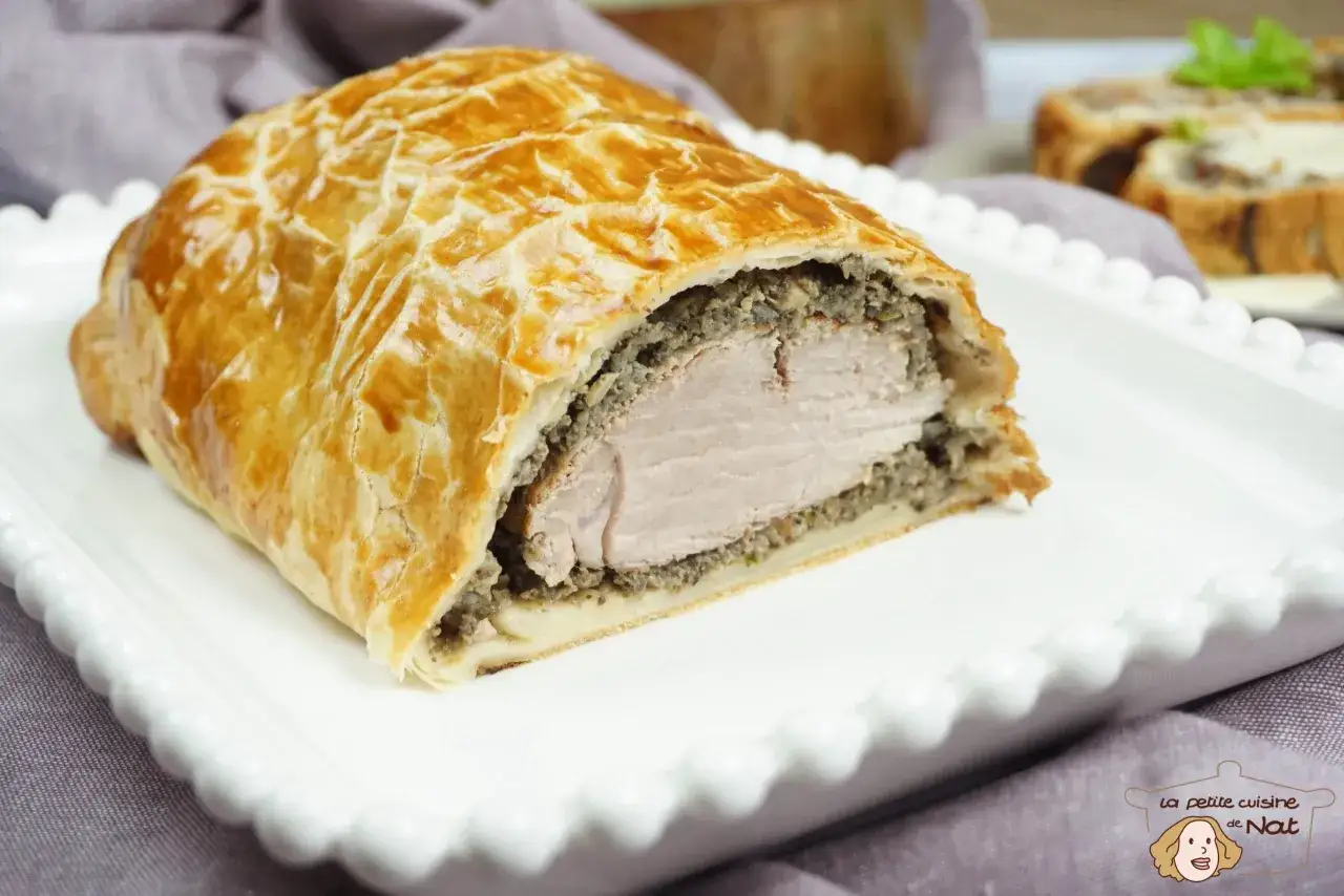Une savoureuse viande en croûte dorée, garnie d'une farce aux champignons, repose sur une assiette blanche.