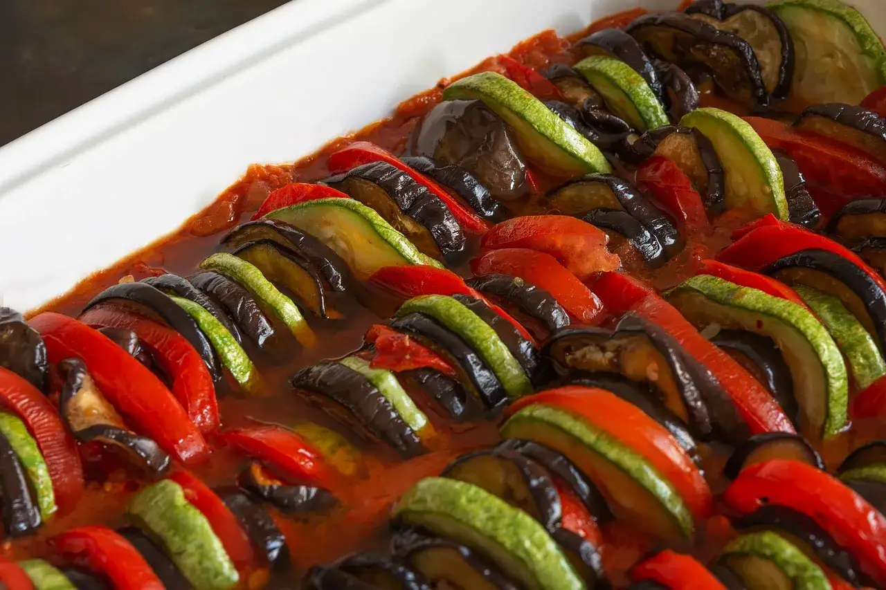 Ratatouille recette : fines tranches d'aubergine, courgette et poivron rouge dispos&eacute;es en &eacute;ventail dans une sauce tomate.