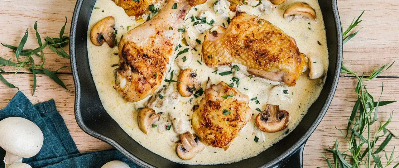 Un plat de poulet à la crème, avec des morceaux de poulet dorés, des champignons et une sauce onctueuse, garni de persil frais.