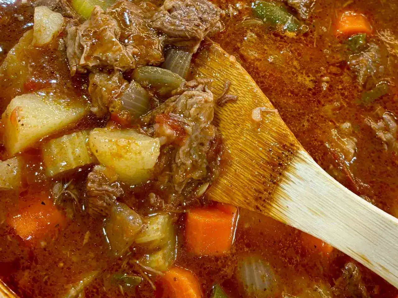 Un plat mijoté réconfortant : quelle viande avec sauce tomate, pommes de terre et carottes, mélangé avec une cuillère en bois.