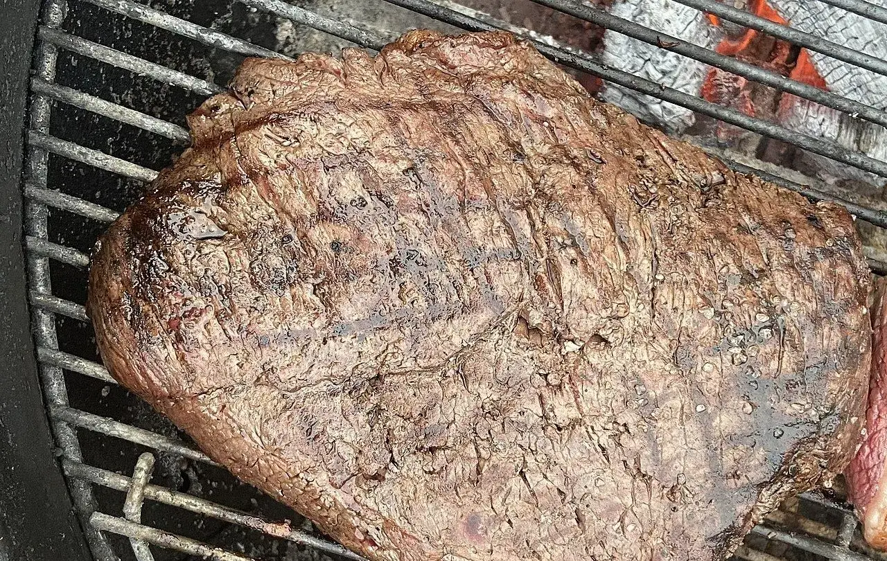 Un morceau de viande juteux cuit sur un barbecue brésilien, avec des marques de grill et des braises ardentes en arrière-plan.