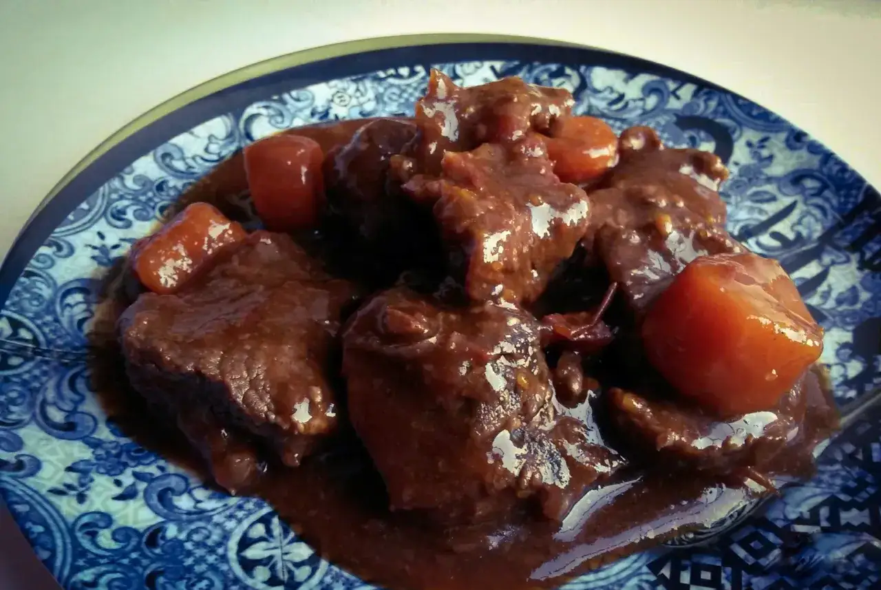 Un plat de joue de bœuf mijotée, tendre et savoureuse, servie avec des carottes dans une sauce riche.