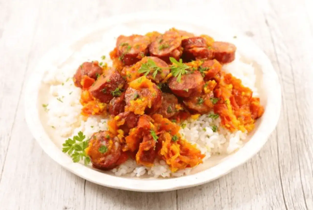 Un plat de rougail saucisse savoureux, avec des rondelles de saucisse épicée sur un lit de riz blanc, garni de persil frais.