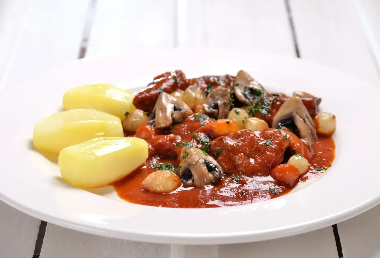 Un plat de veau marengo traditionnel, mijoté dans une sauce tomate riche avec des champignons et des oignons, servi avec des pommes de terre vapeur.