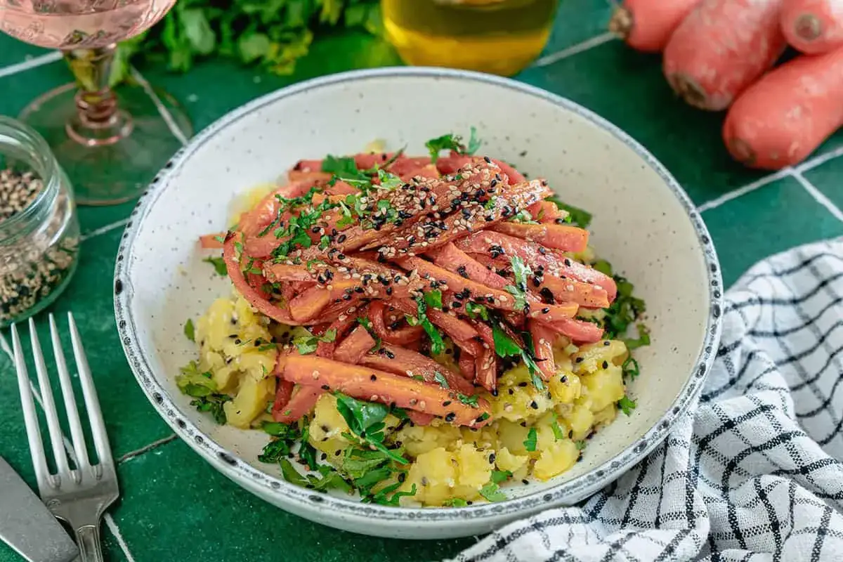 Un plat color&eacute; avec une pur&eacute;e de carotte r&acirc;p&eacute;e, garnie de graines de s&eacute;same et de persil frais, sur un lit de pommes de terre &eacute;cras&eacute;es.