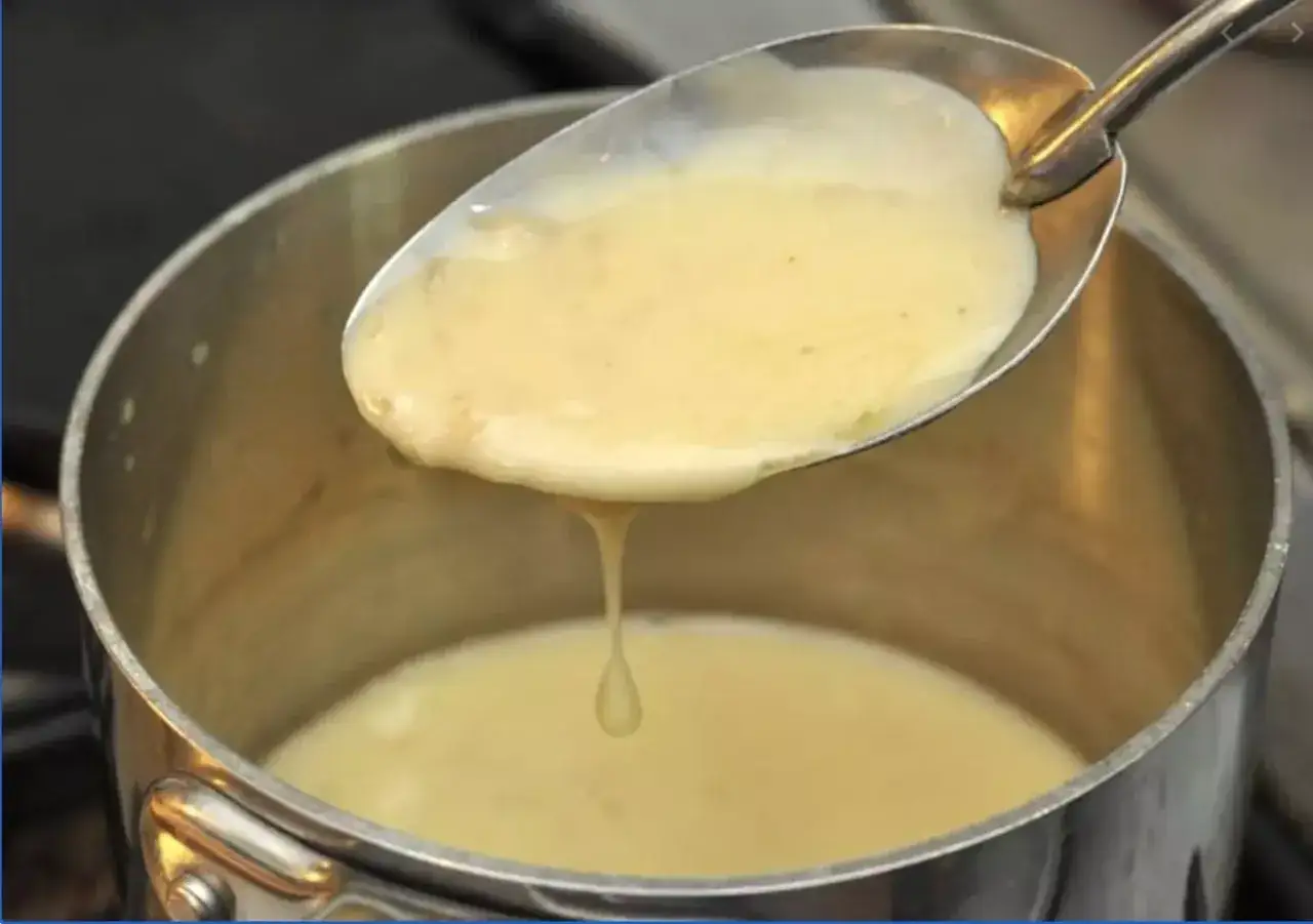 Une cuillère de sauce onctueuse, prête pour une recette de beurre blanc. La sauce coule doucement dans la casserole.