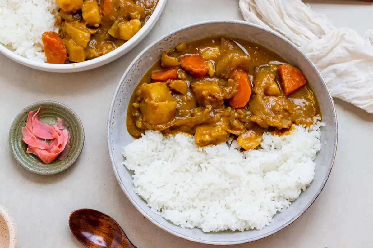 Deux bols de curry japonais savoureux avec du riz blanc et des carottes. Une petite coupelle de gingembre mariné rose complète ce plat réconfortant.