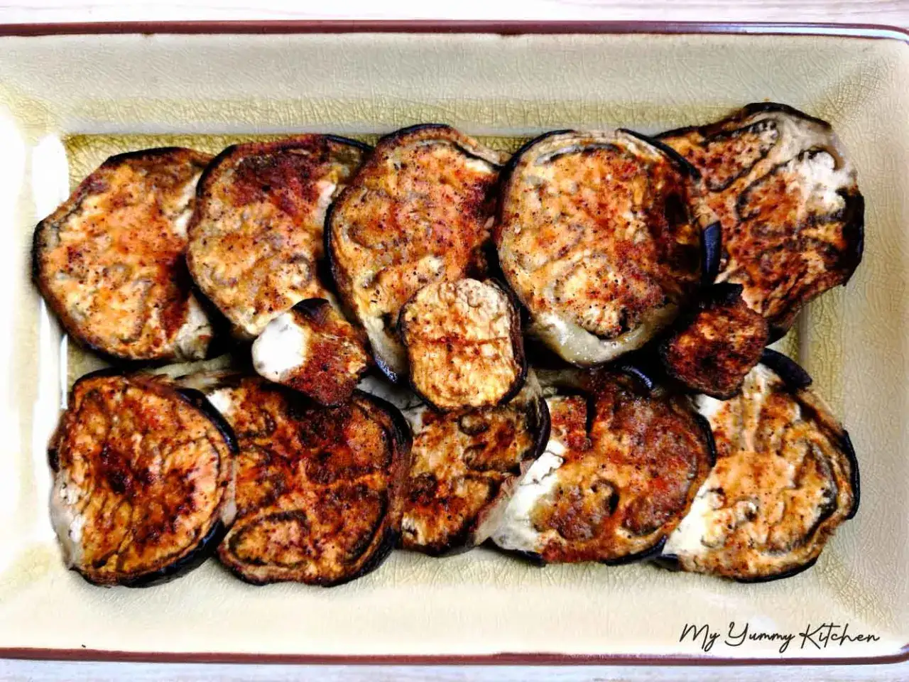 Tranches d'aubergine au four, dorées et légèrement caramélisées, disposées dans un plat. Un délice simple et savoureux.