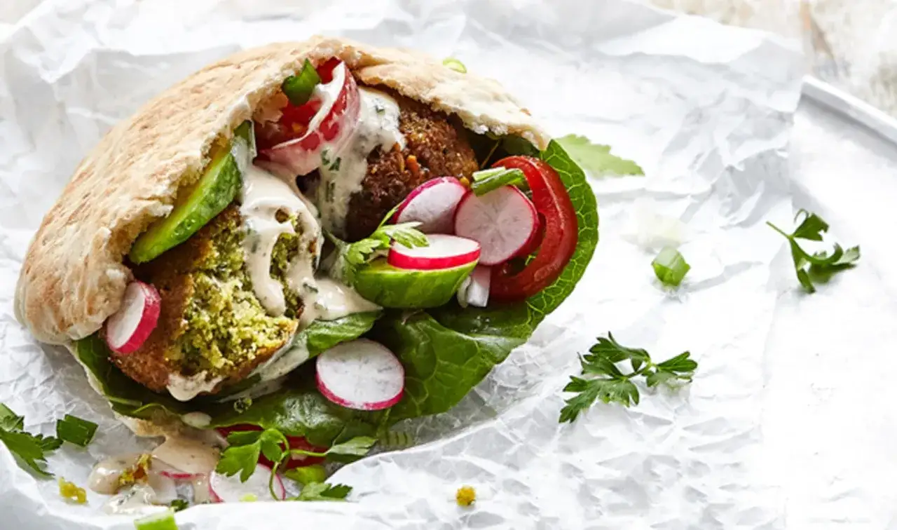 Un d&eacute;licieux falafel recette dans un pain pita garni de l&eacute;gumes frais et de sauce tahini.