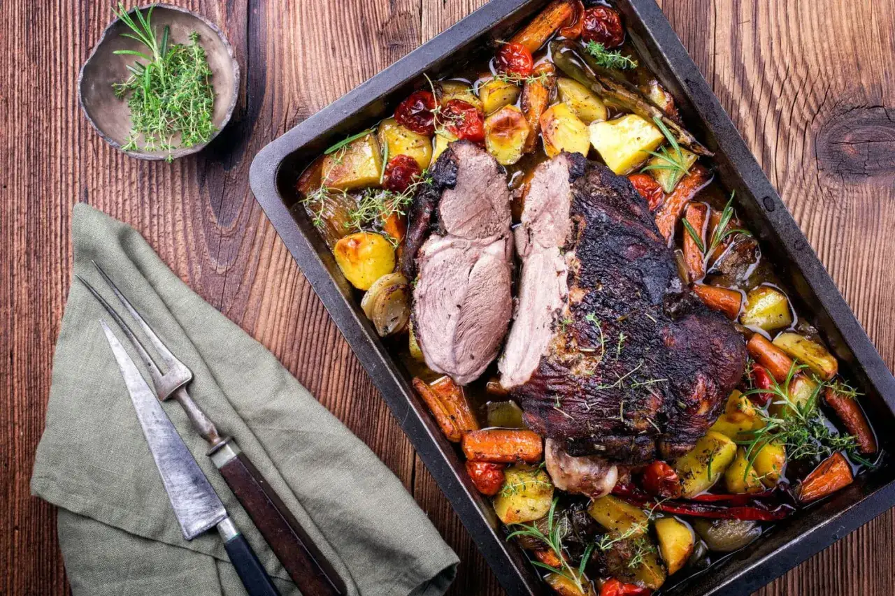 Gigot d'agneau tendre rôti avec pommes de terre, carottes et tomates cerises, garni de romarin frais. Un délice à partager.