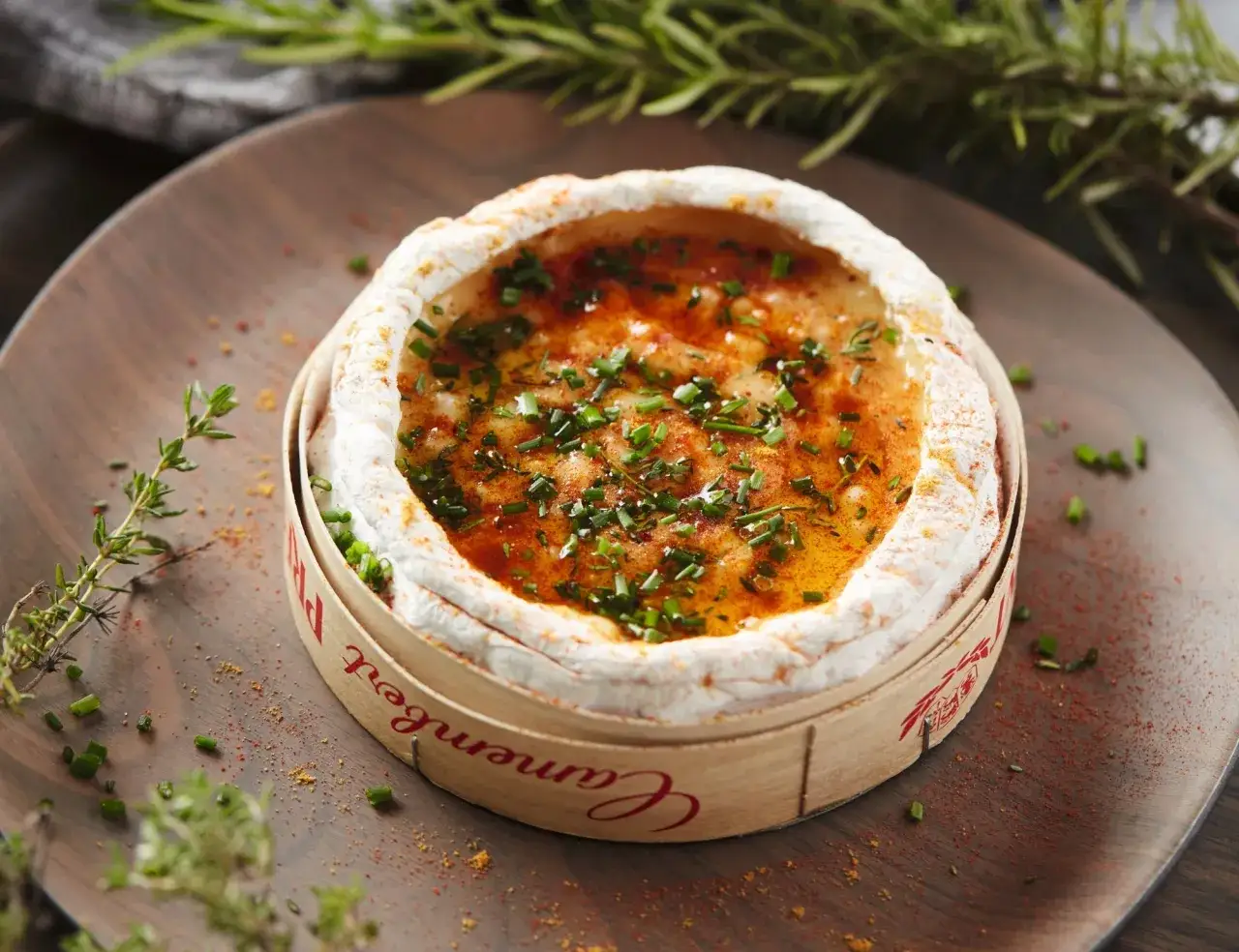 Camembert au barbecue gaz, fondant et garni de ciboulette et d'épices, prêt à être dégusté sur une assiette en bois.