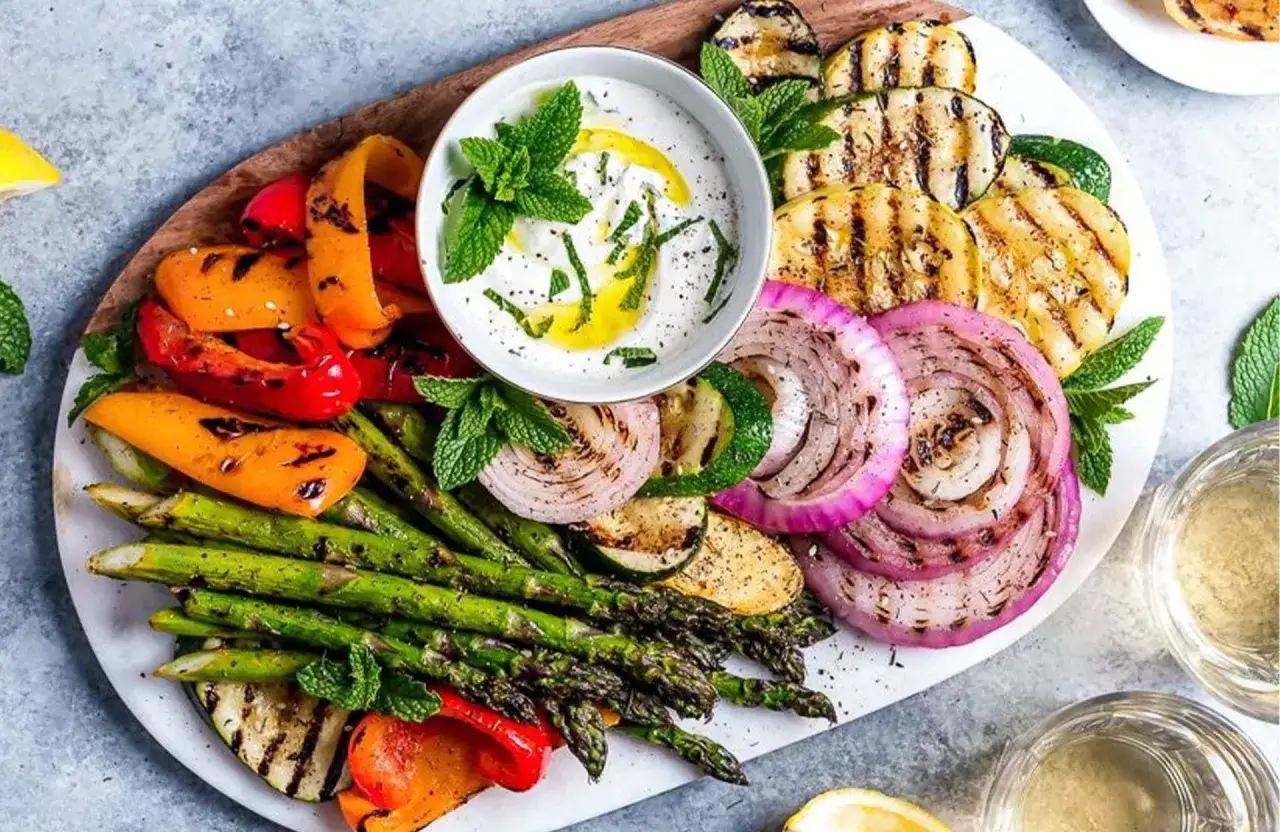Assiette de légumes grillés colorés, parfaite pour une recette végétarienne. Poivrons, courgettes, oignons rouges et asperges accompagnés d'une sauce blanche à la menthe.