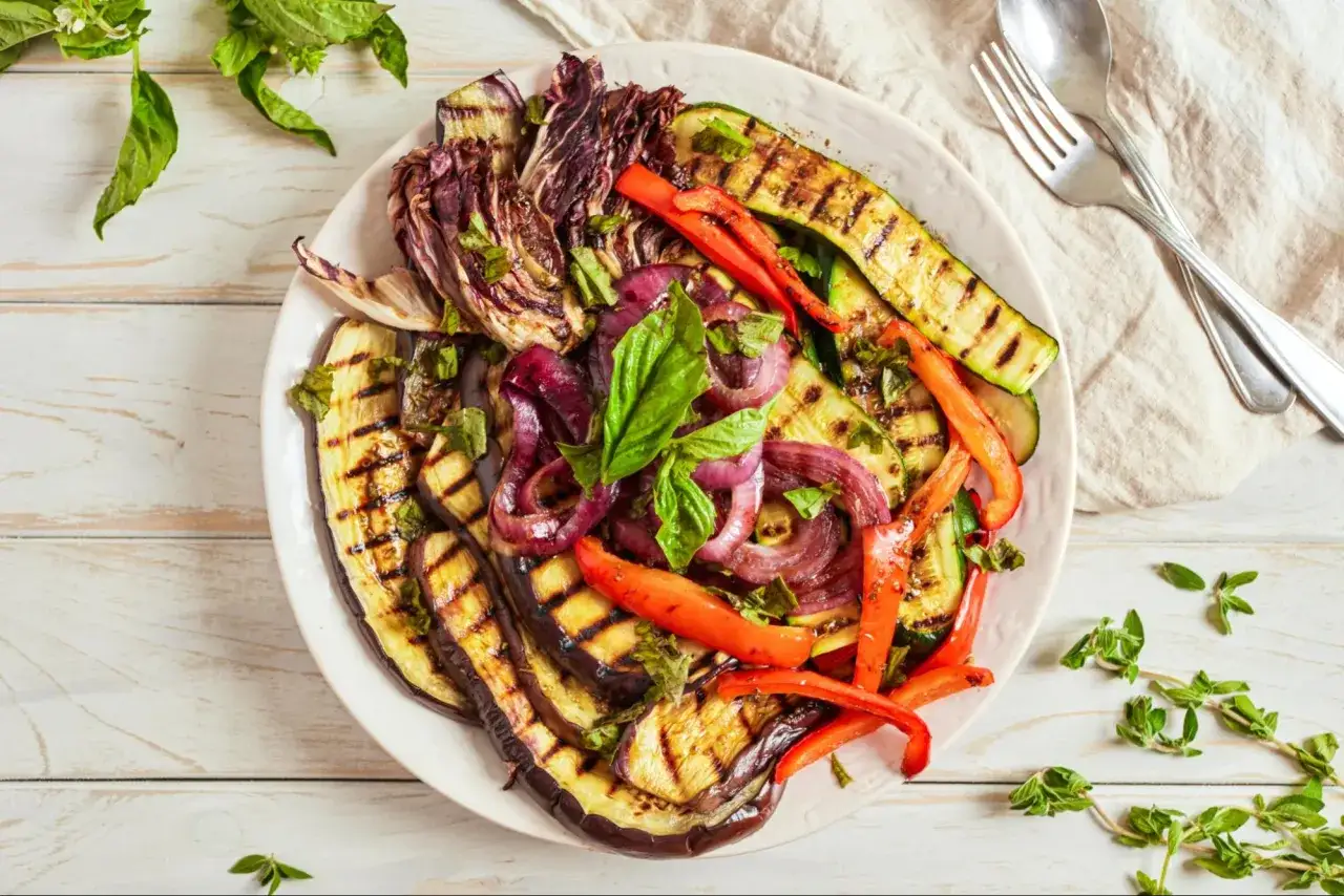 Assiette de légumes grillés, un délice de barbecue italien : aubergines, courgettes, poivrons rouges, oignons et radicchio, parsemés de basilic frais.