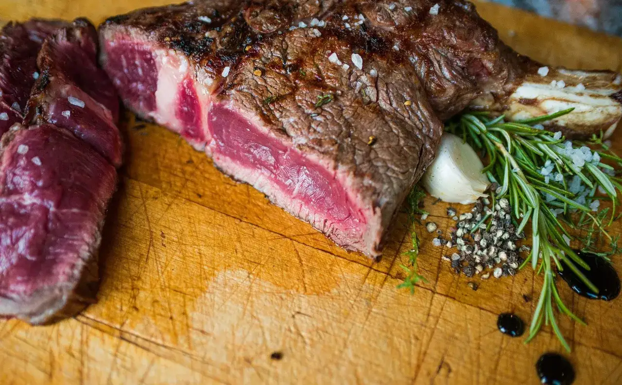 Une belle côte de bœuf juteuse, tranchée et assaisonnée de gros sel, poivre, ail et romarin sur une planche en bois.