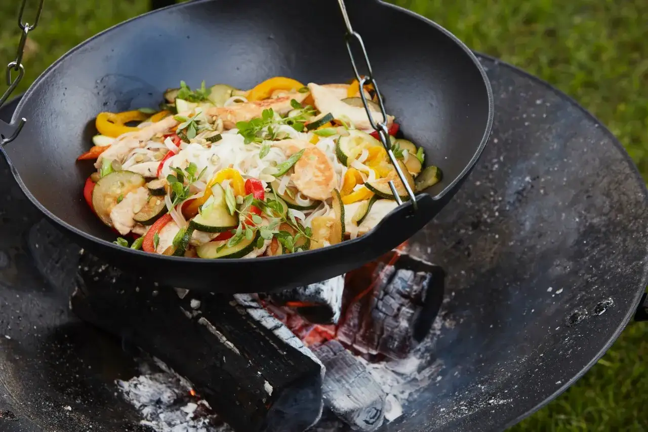 Un délicieux plat de poulet et légumes sautés dans un wok sur un feu de bois, parfait pour un repas en plein air au bbq.