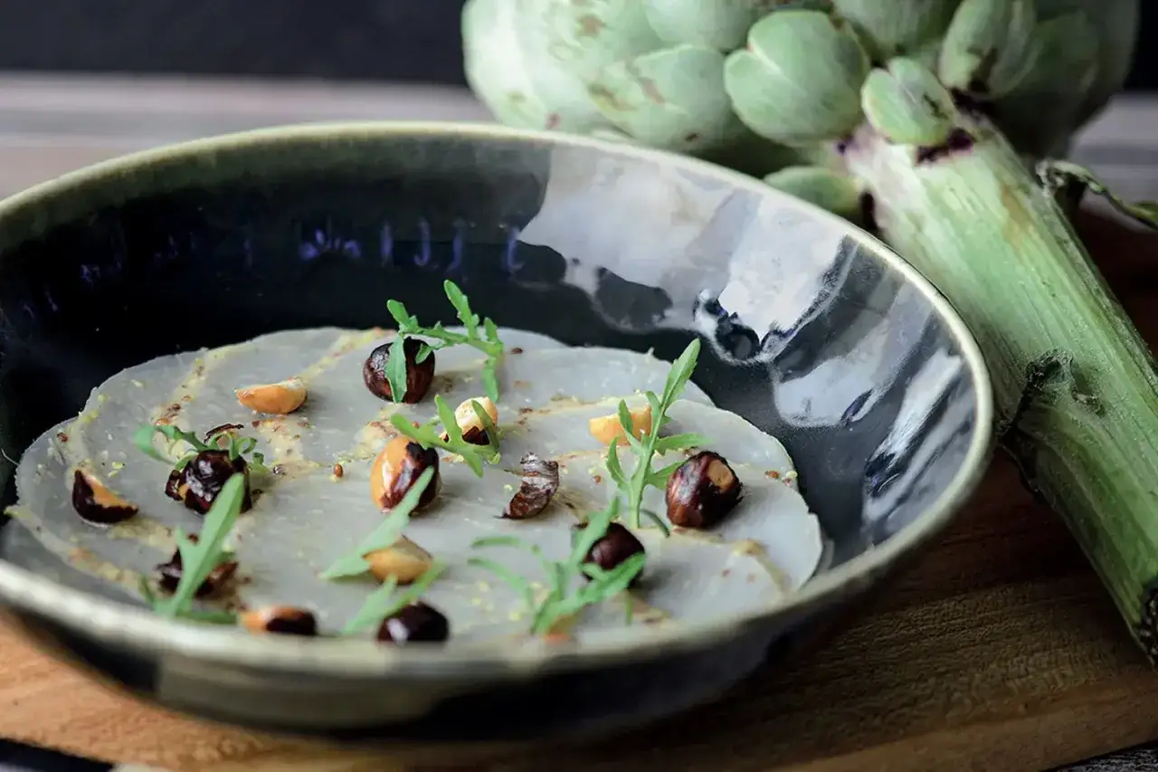 Carpaccio d'artichaut, une recette légère et raffinée, garnie de noisettes torréfiées et de roquette fraîche.