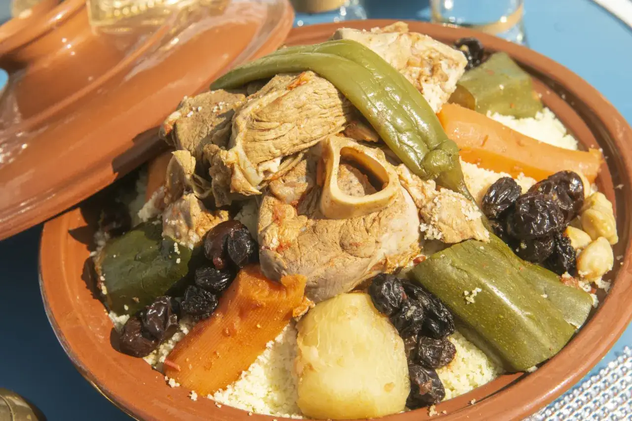 Un plat de couscous algérien généreux avec viande, légumes et raisins secs, servi dans un plat en terre cuite.