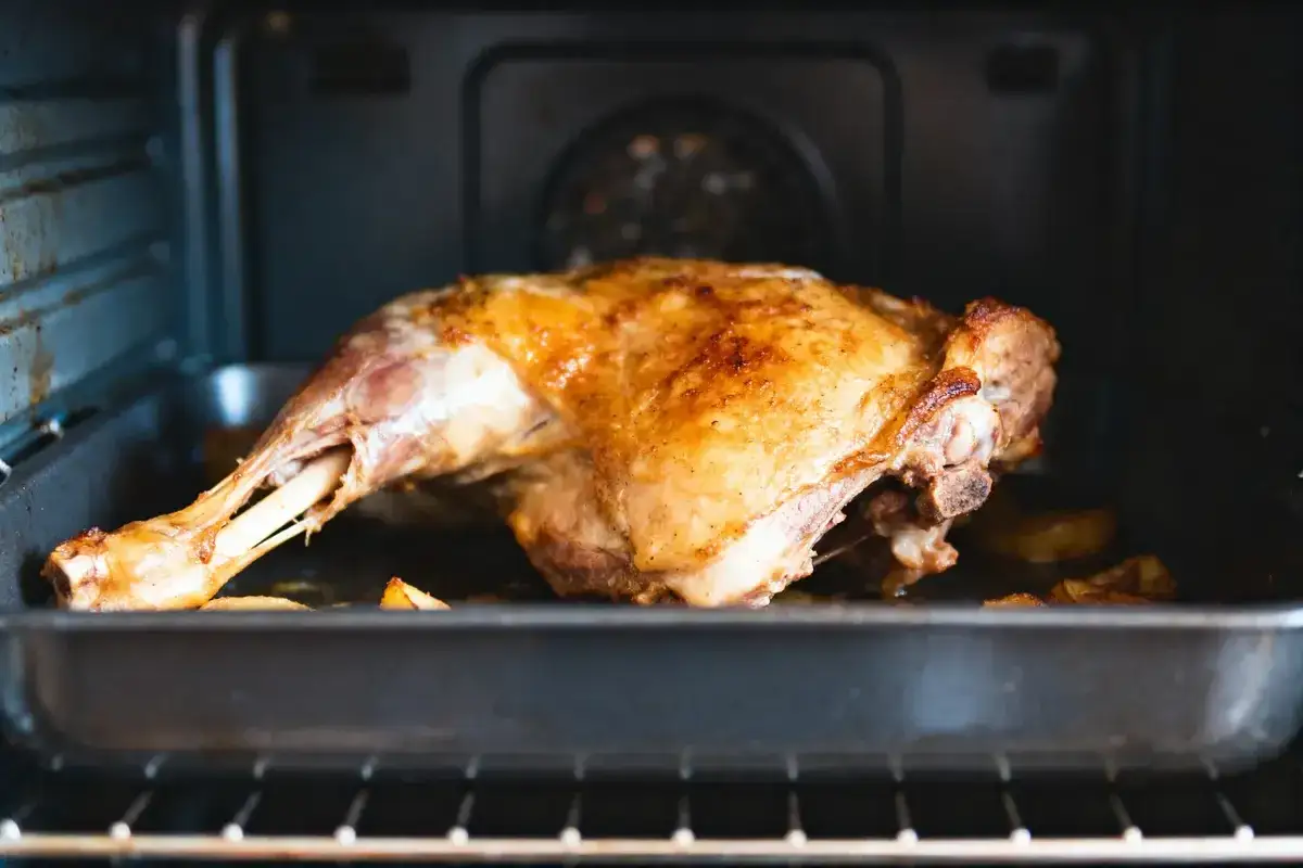 Gigot d'agneau doré et juteux, prêt à régaler 8 personnes. Il cuit doucement dans un plat au four, entouré de pommes de terre rôties.