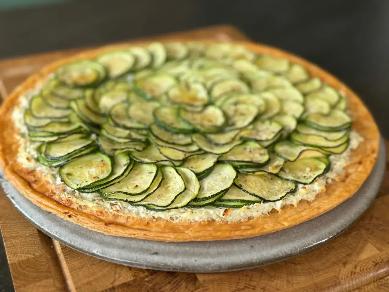 Tarte courgette aux fines rondelles de courgettes disposées en rosace sur une garniture crémeuse, sur une pâte feuilletée dorée.