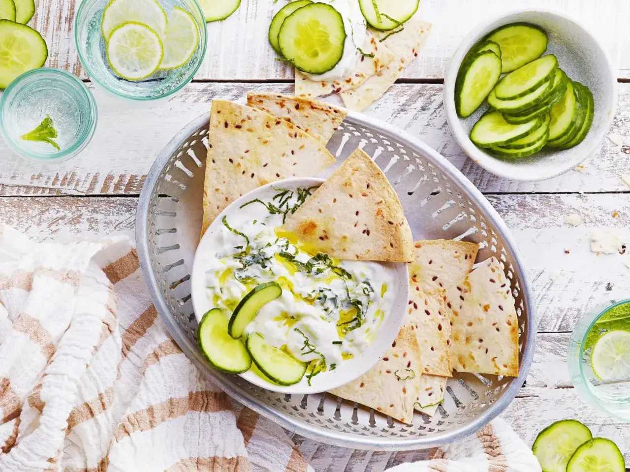Un bol de tzatziki crémeux avec des tranches de concombre et des pains plats croustillants. Parfait pour une recette facile et rafraîchissante.